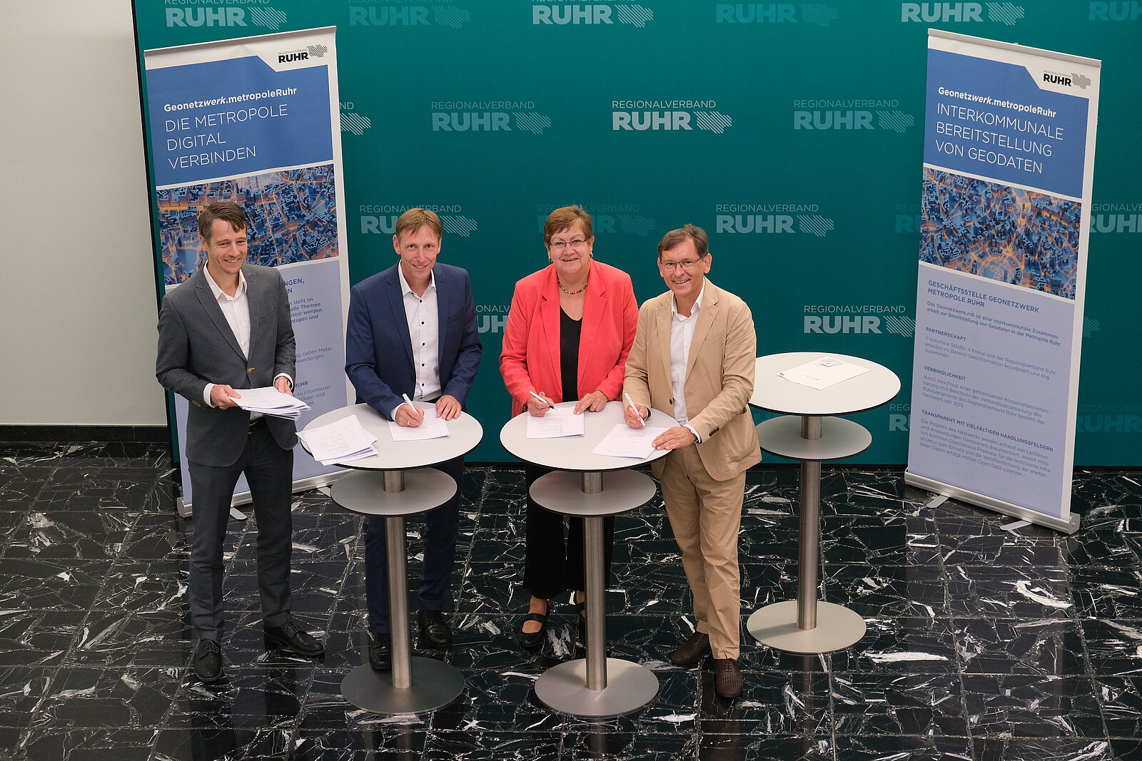 Vertragsunterzeichnung 4 Personen an Stehtischen in einem Foyer vor einer grünen Wand. Personen von rechts nach links: Dr. Frank Dudda, Vorsitzender der RVR-Verbandsversammlung, RVR-Regionaldirektorin Karola Geiß-Netthöfel, Ulf Meyer-Dietrich, Stadt Dortmund und derzeitiger Lenkungskreissprecher, Andreas Weßel, RVR-Referatsleiter